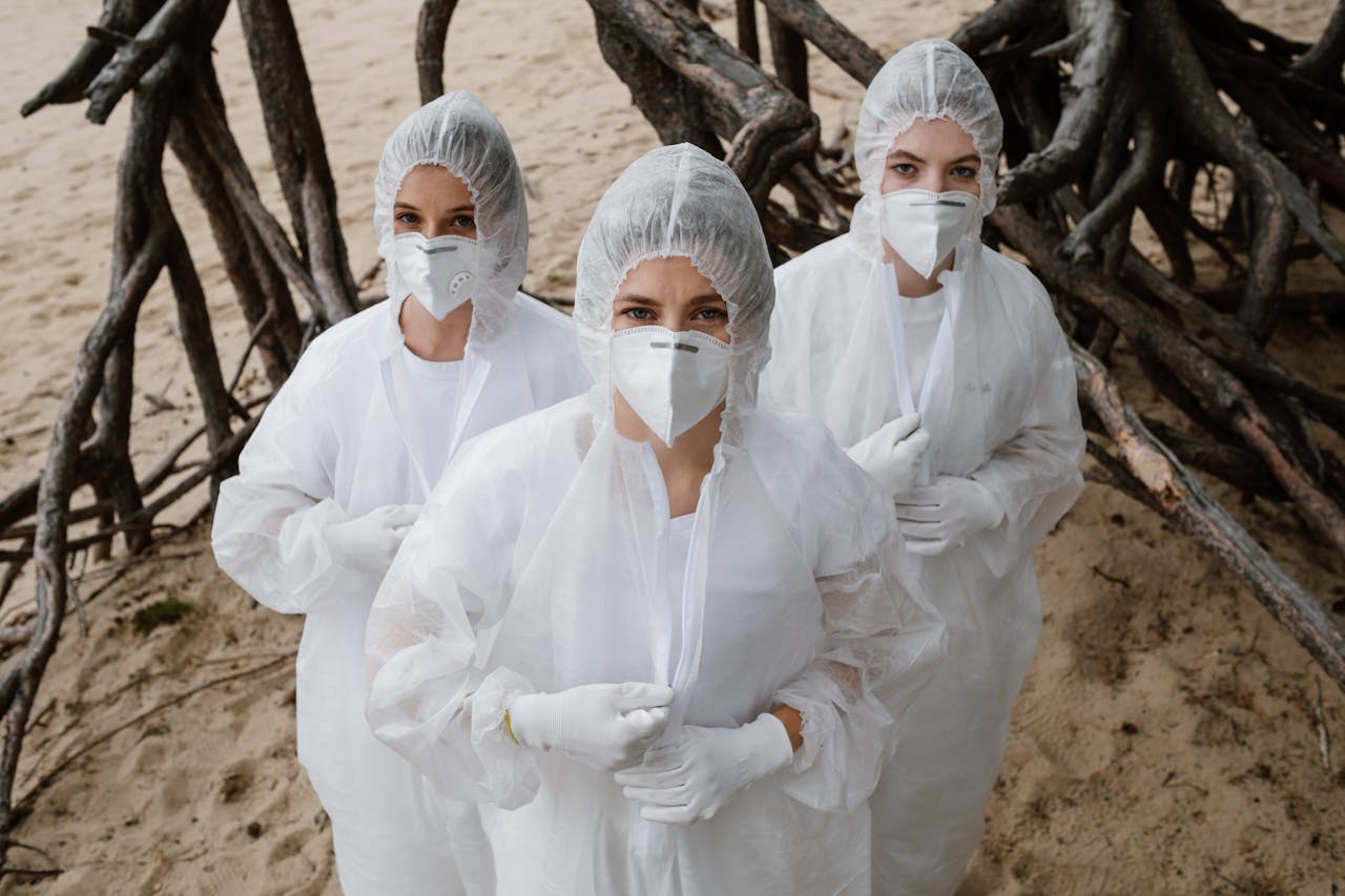 Three women volunteers in protective suits and masks on a beach, focusing on environmental conservation.