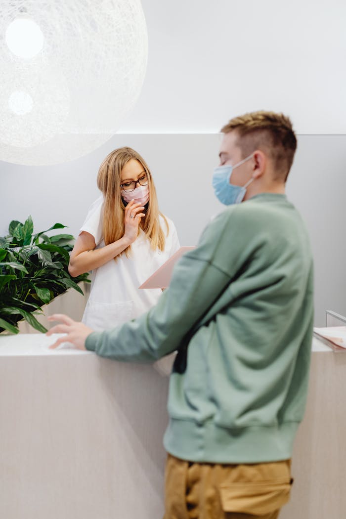 A man and a woman wearing face masks interact at an office reception counter.
