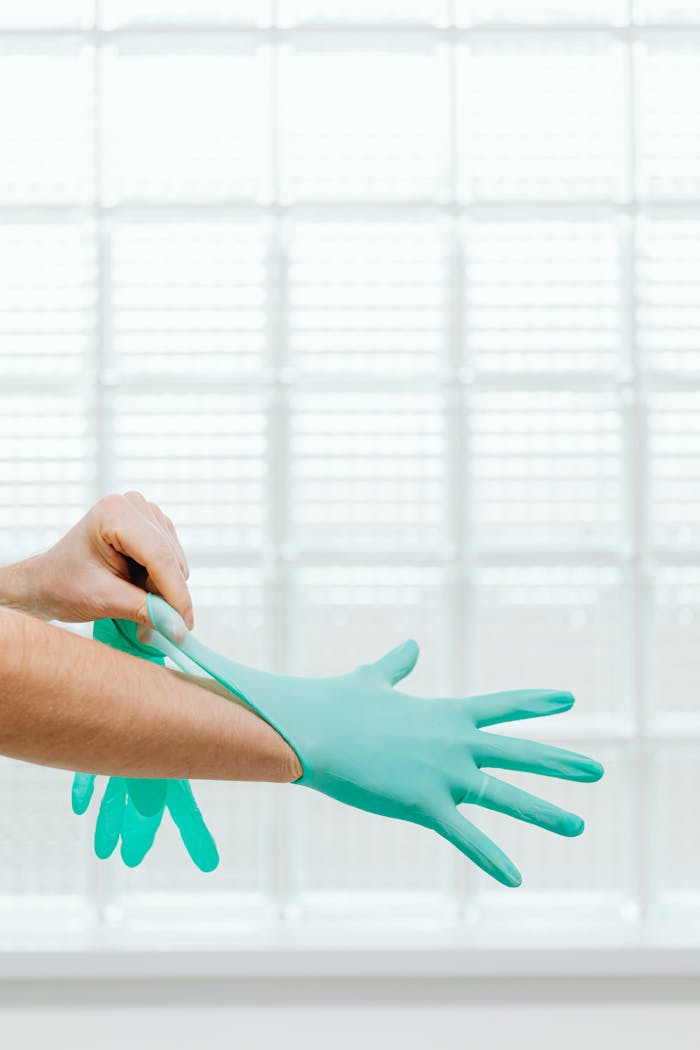 Close-up of a healthcare professional wearing teal gloves against a bright background.